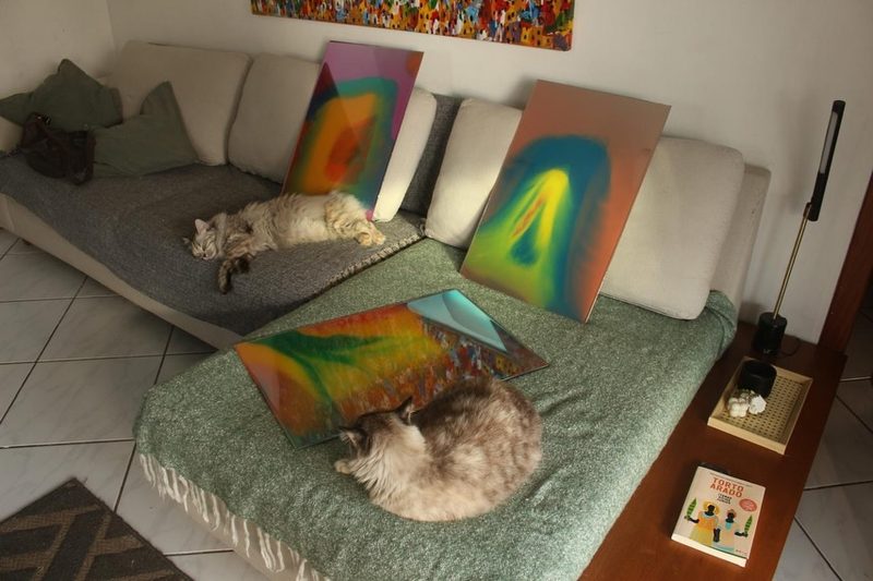 Três espelhos retangulares coloridos apoiados num sofá, com dois gatos dormindo ao lado.